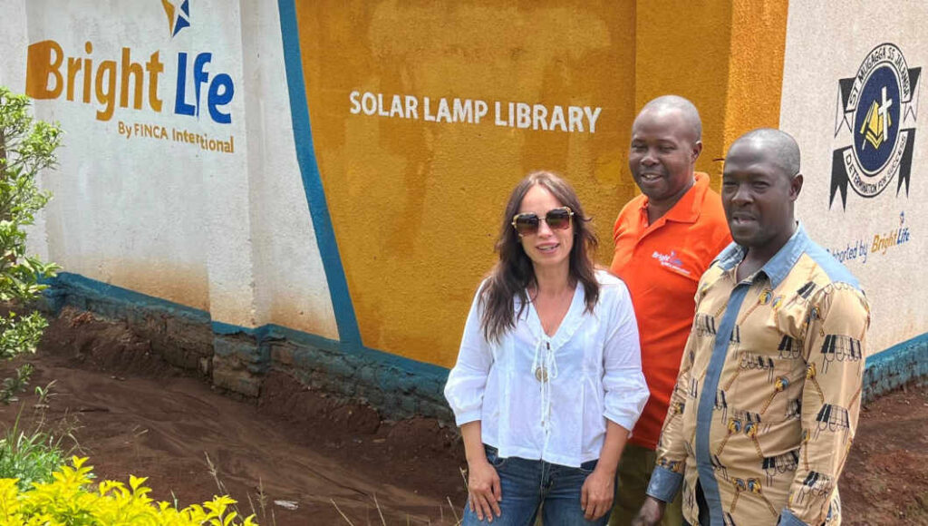 Iris stands with BrightLife staff person Siraje and Headmaster John Ssemtomko at one of the school's supported by FINCA's Lamp Library project.